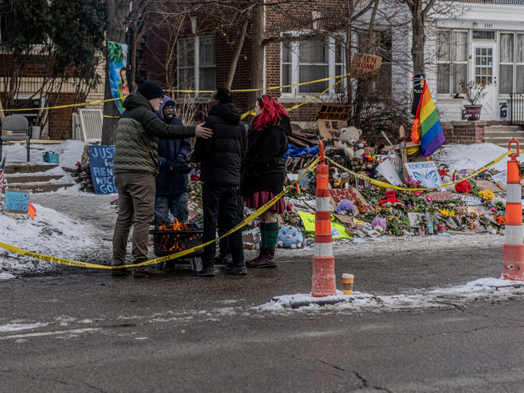 Community members and visitors huddled around an open pit fire at the Renee Good Roadside Memorial in Minneapolis to keep warm during a winter vigil for the slain mother of three, ages 15, 12, and 6. (Photo by Awe Video & Photo Studio)